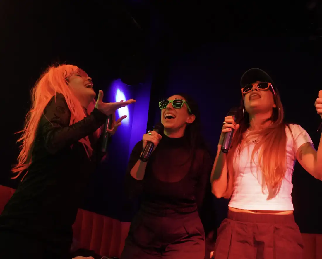 Tres amigas cantando juntas con micrófonos en LAF CLUB
